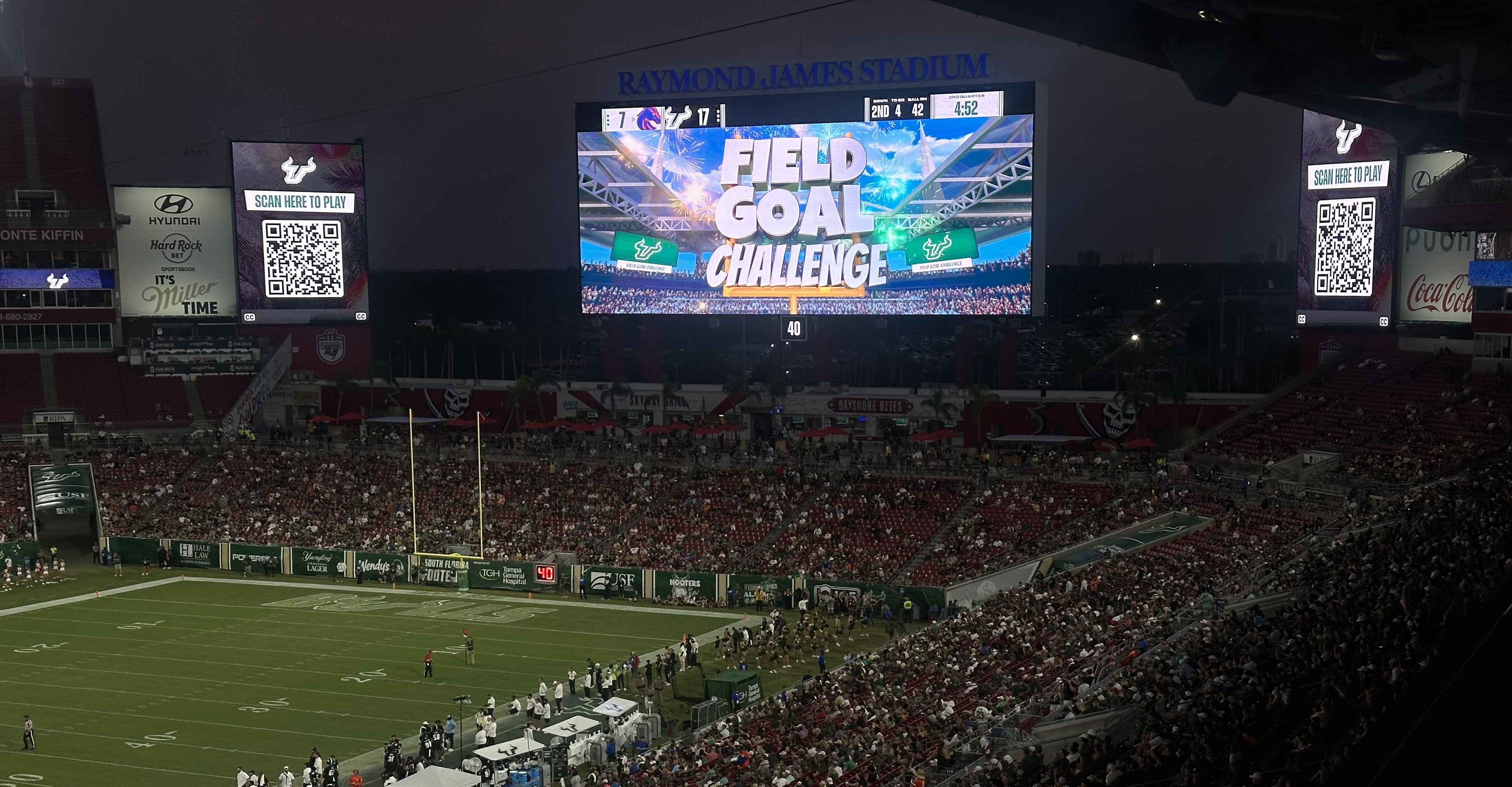 Packed football stadium at night featuring a large video board displaying a venue4D interactive Field Goal Challenge game, with QR codes for real-time fan participation.